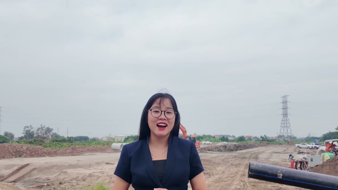 Em Hoa đứng trên công trường đại lộ Đông Tây ở Hưng Yên, phía sau là máy xúc, ống cống và cột điện cao thế
