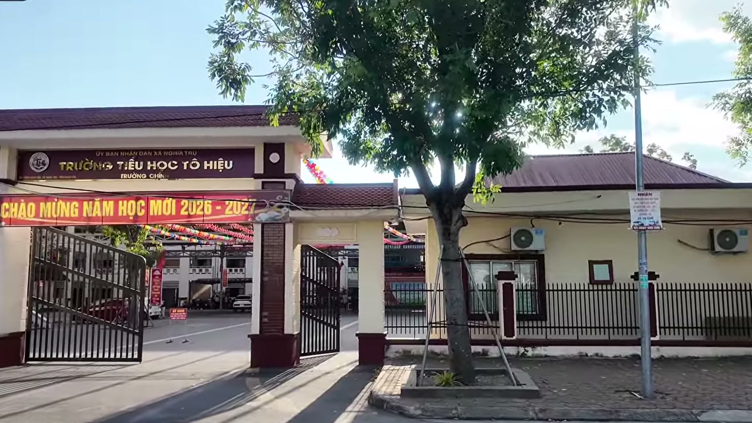 Cổng Trường Tiểu học Tô Hiệu treo băng rôn chào mừng năm học mới, cờ đỏ hai bên đường
